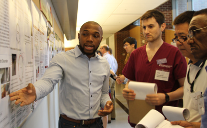 Incoming D1 student Chimdi Ego-Osuala presents his research to the judges panel during the poster competition held July 28.