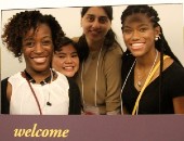 Four students smile while holding up a welcome sign