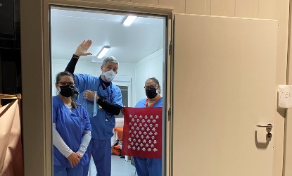 Three volunteer dentists in Ukraine wave from a shipping container