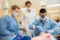 A teacher oversees two students performing a dental procedure