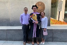 Dan Yang poses in his graduation gown, accompanied by family