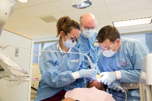 Photo of two students performing a pediatric dental procedure while an instructor oversees them
